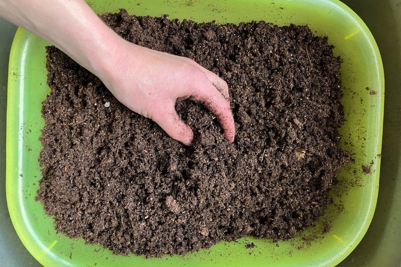 Hand mixing potting soil in a yellow plastic tub