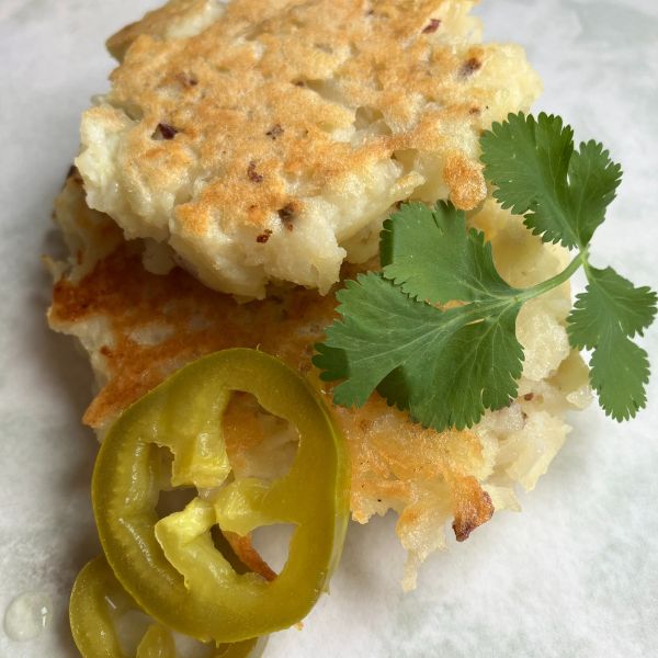 Two potato pancakes stacked on top of each other with a pickled jalapeno and cilantro garnish