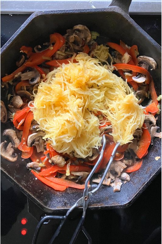Spaghetti squash noodles and chopped celery, red pepper, and mushrooms sauteing in a cast iron skillet with metal tongs