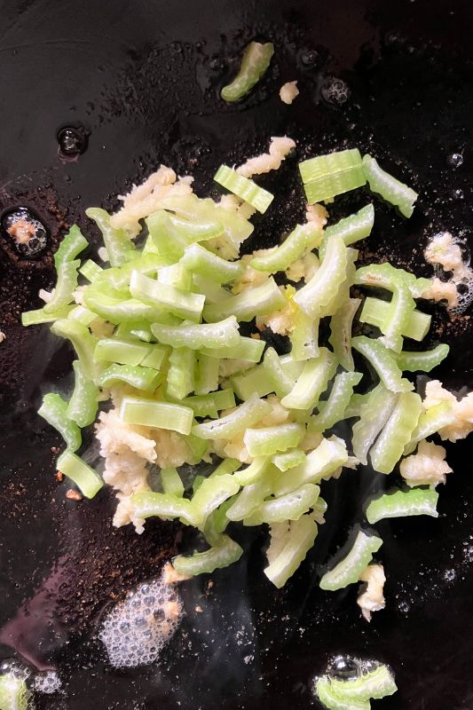 Chopped celery and garlic sautéing in butter on a cast iron frying pan