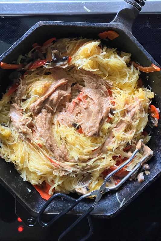 Peanut butter sauce being stirred into stir fried spaghetti squash noodles and chopped bell peppers, celery, and mushrooms